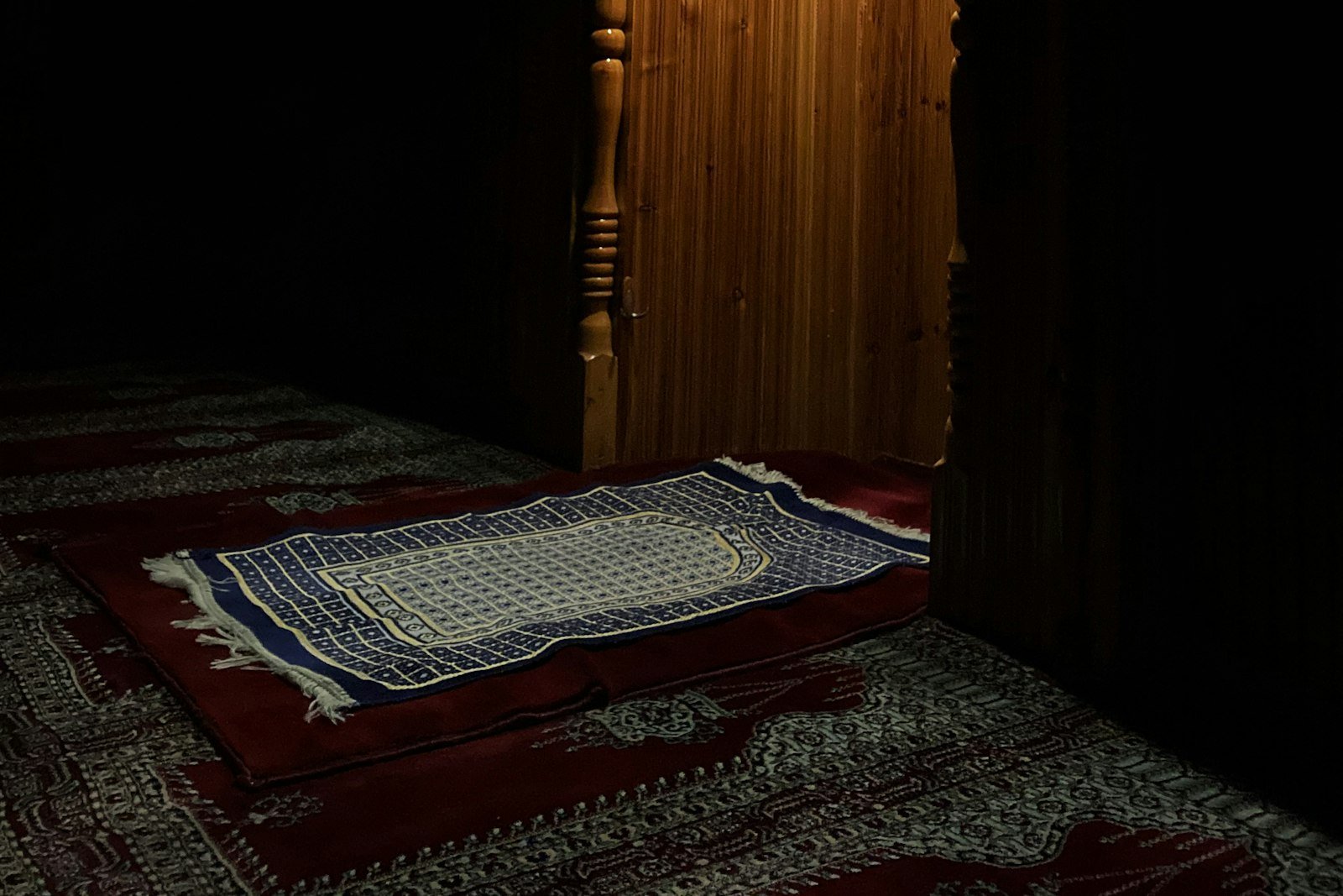 Yatsı sonrası loş mihrap önünde seccade — caminin sessiz hâli